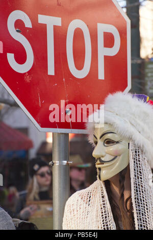 ASHEVILLE, North Carolina, Stati Uniti d'America - 7 febbraio 2016: giovane donna che indossa una maschera di Guy Fawkes sorge da un segnale di STOP nel 2016 Mardi Gras Parade Foto Stock