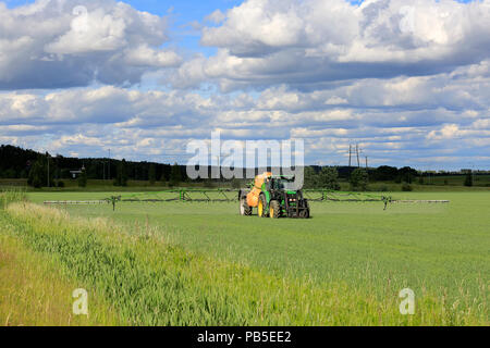 Agricoltore spruzza campo di grano con trattore John Deere e Amazone 5200 UX Irroratrice montata su una bella giornata d'estate. Salo, Finlandia - 8 giugno 2018. Foto Stock