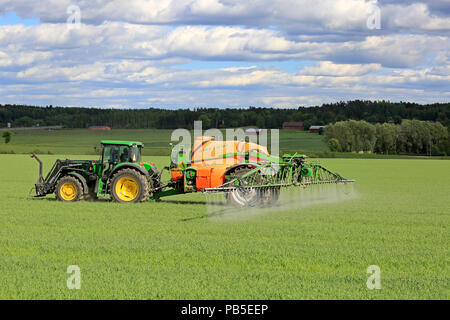 Agricoltore spruzza campo di grano con trattore John Deere e Amazone 5200 UX Irroratrice montata su una bella giornata d'estate. Salo, Finlandia - 8 giugno 2018. Foto Stock