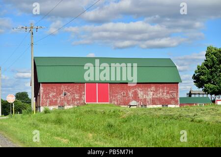 Burlington, Illinois, Stati Uniti d'America. Un vecchio weathered granaio rosso dotato di nuove porte di metallo e un tetto verde. Foto Stock