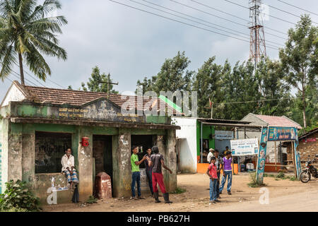 Naralapura, Karnataka, India - 1 Novembre 2013: ragazzi, adolescenti e il vecchio uomo di attendere al calcestruzzo sporco il trasporto pubblico rifugio nel villaggio. Caffè sh Foto Stock