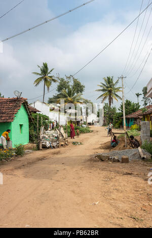 Naralapura, Karnataka, India - 1 Novembre 2013: vista sul marrone principale strada sterrata sul villaggio con poche case, le donne con bambini di fronte a loro. Gree Foto Stock