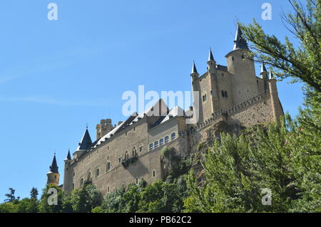 Castello Alcazar visto dal fiume che scorre attraverso la valle che regna in Segovia leggermente catturati da un boschetto. Architettura, Viaggi, storia Foto Stock