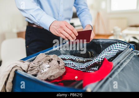 L'uomo la preparazione per il viaggio d'affari. Aprire traveler del sacco con passaporto, abbigliamento e accessori. Viaggi e vacanze concetto. Foto Stock