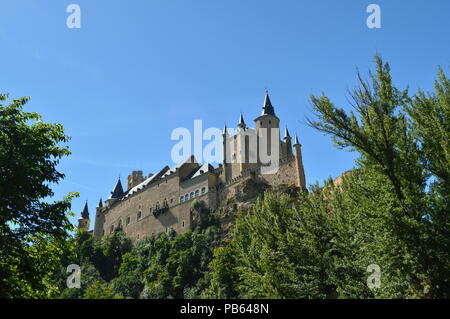 Castello Alcazar visto dal fiume che scorre attraverso la valle che regna in Segovia leggermente catturati da un boschetto. Architettura, Viaggi, storia Foto Stock