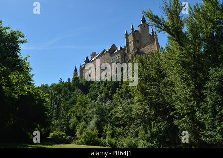 Castello Alcazar visto dal fiume che scorre attraverso la valle che regna in Segovia leggermente catturati da un boschetto. Architettura, Viaggi, storia Foto Stock