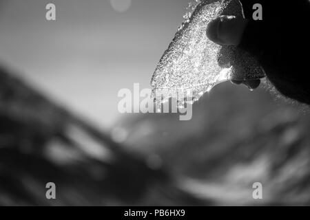 Mano che tiene un pezzo di ghiaccio rotto fino al sole Foto Stock