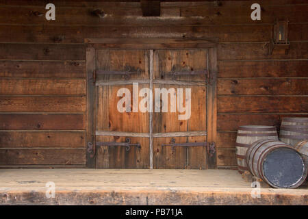 Legno vecchio porte doppie con rusty weathered hardware, botti di legno impilate accanto a porta. Foto Stock