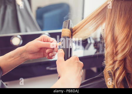 Parrucchiere facendo un'acconciatura per client con un ferro arricciacapelli in salone di bellezza Foto Stock