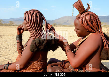 Le donne himba trecciatura reciprocamente i capelli. Marienfluss Valley. Kaokoland, Namibia Ottobre 2015 Foto Stock