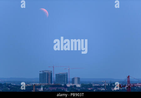 Monaco di Baviera, Germania. 27 Luglio, 2018. La luna che sorge può essere visto nella foschia su Monaco di Baviera. Durante la più lunga eclissi lunare del XXI secolo, la luna si tuffa nel cono d'ombra della Terra. Credito: Matthias esitano di fronte/dpa/Alamy Live News Foto Stock