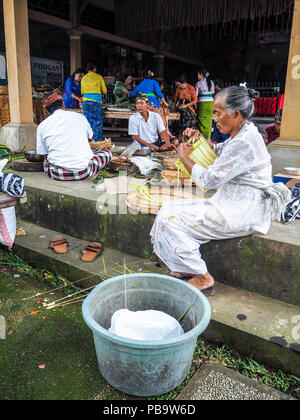 Ubud, Bali - Aprile 2017: vecchia donna fare bambù cestelli chiamati canang sari per il Nyepi festival in un tempio locale Foto Stock