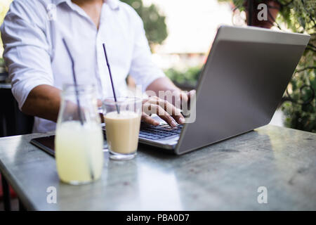 Giovani attraenti Afro American businessman in seduta cafe bar, a bere caffè e facendo qualche lavoro sul computer portatile. Foto Stock