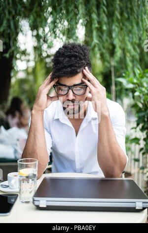 Giovani attraenti Afro American businessman in seduta cafe bar, a bere caffè e facendo qualche lavoro sul computer portatile. Foto Stock
