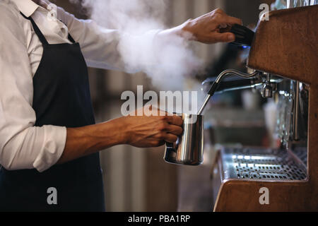 Coffee shop lavoratore preparazione di caffè su steam macchina per caffè espresso. Ritagliato colpo di uomo che lavora in una caffetteria di indossare un grembiule. Foto Stock