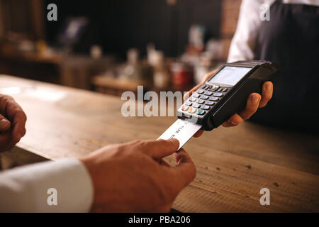 Il cliente inserisce la sua carta di credito nella macchina per il pagamento presso il cafe. Il cliente paga per loro ordine con una carta di credito in un caffè con il barista hol Foto Stock