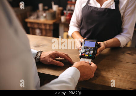 Ritagliato shot dei maschi di cliente di pagare per un caffè con carta di credito presso il cafe. Donna barista tenendo un lettore di carte di credito macchina con uomo che fa il pagamento su c Foto Stock