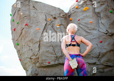 Foto dal retro dello sport bionda con sacchetto contro rock boulder durante il giorno Foto Stock