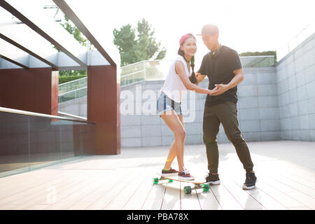 Giovane uomo cinese ad insegnare la sua fidanzata per skateboard Foto Stock