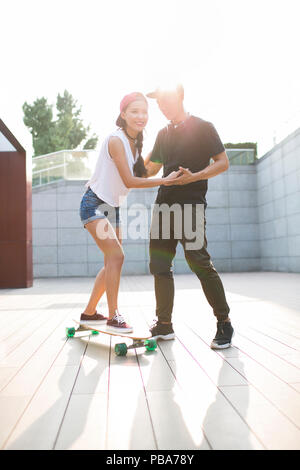 Giovane uomo cinese ad insegnare la sua fidanzata per skateboard Foto Stock