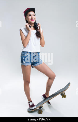 Allegro giovane donna cinese con le cuffie lo skateboard Foto Stock