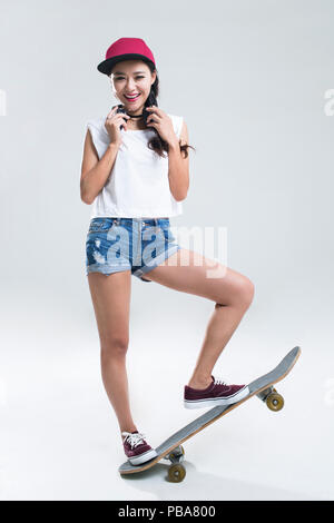 Ritratto di Allegro giovane donna cinese con le cuffie lo skateboard Foto Stock