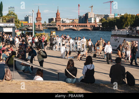 Persone, rilassanti passeggiate sul fiume Spree bank, Berlino skyline, Oberbaum Bridge e il fiume Sprea panorama Foto Stock
