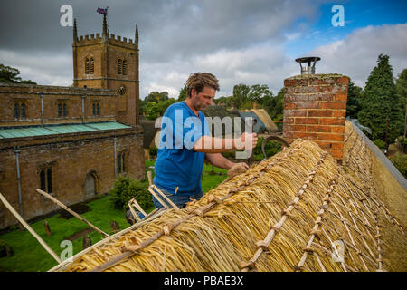 Dan Quatermain, master thatcher, lavorando su un tetto di paglia in Wroxton village, Oxfordshire, Regno Unito. Settembre 2015. Foto Stock