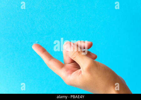 Lente a contatto sul dito su sfondo blu Foto Stock