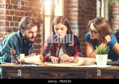 Equipaggio di giovani designer professionisti a discutere le idee circa il blueprint durante la riunione di loft ufficio moderno Foto Stock