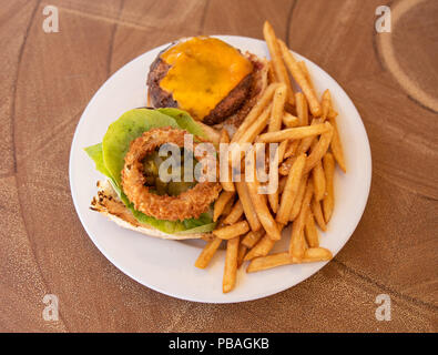 Cheeseburger con patatine fritte e insalata su piastra bianca Foto Stock