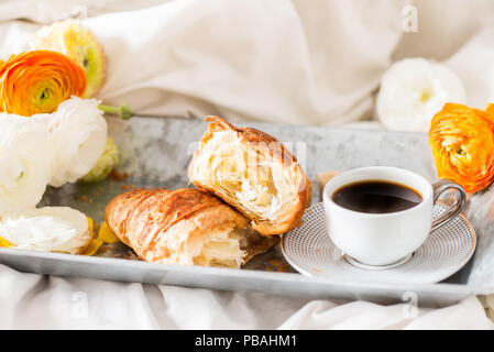La prima colazione a letto da croissant fresco e la tazza di caffè sul vassoio grigio, ranuncoli fiori nelle vicinanze Foto Stock