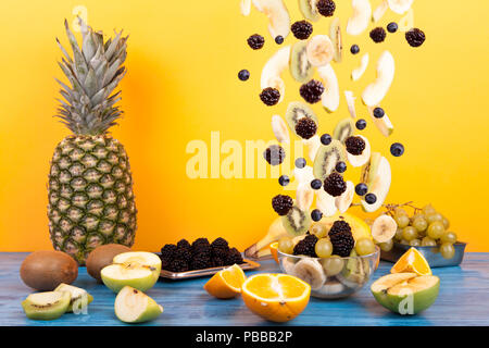 Flying frutta a fette in recipiente di vetro con insalata di frutta su uno sfondo giallo. Composizione della dieta sana Foto Stock