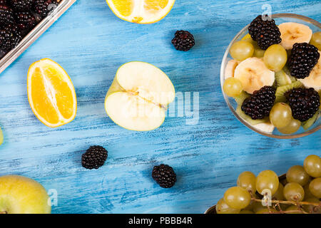 Fette di frutta a bacca e vista sul blu sullo sfondo di legno. Un tavolo di legno con fresca frutta tropicale. Natura sana freschezza mix di frutta Foto Stock