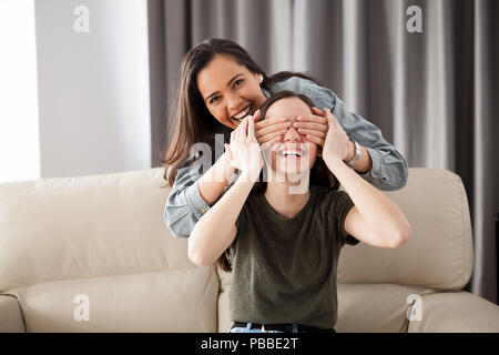 Due amiche stanno giocando a nascondino sul divano del soggiorno Foto Stock