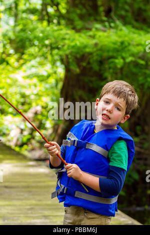 Un esasperato little boy guarda la telecamera in frustrazione perché la sua canna da pesca è catturato in una struttura ad albero. Vi è il sudore gocciolamento verso il basso il lato di h Foto Stock