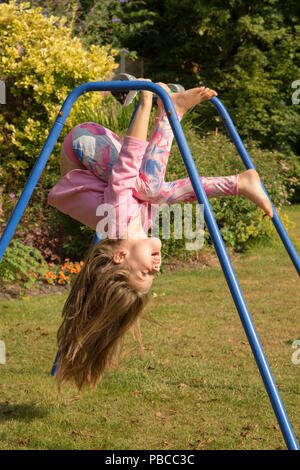 6 anno vecchia ragazza ginnastica fare acrobazie su un apparato nel giardino sul retro per giocare, UK. Foto Stock