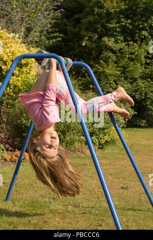 6 anno vecchia ragazza ginnastica fare acrobazie su un apparato nel giardino sul retro per giocare, UK. Foto Stock