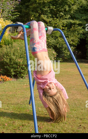 6 anno vecchia ragazza ginnastica fare acrobazie su un apparato nel giardino sul retro per giocare, UK. Foto Stock