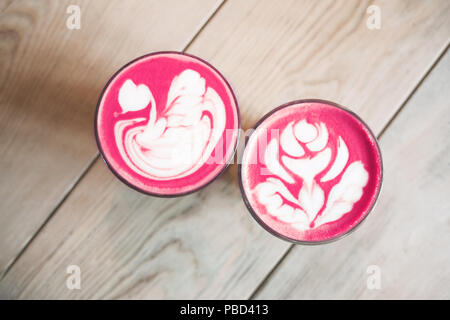 Sana barbabietola alla moda del latte con latte art in due bicchieri sul tavolo di legno. Vista dall'alto. Foto Stock