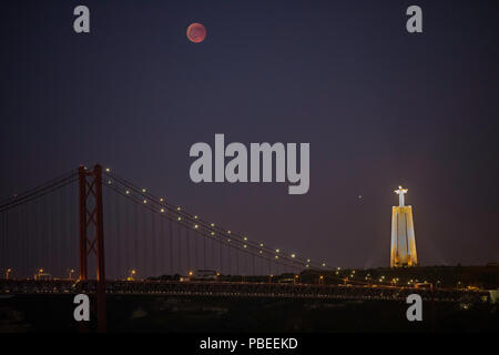 Lisbona, Portogallo. Il 27 luglio 2018. La più lunga eclissi lunare totale del XXI secolo, noto anche come la luna di sangue nella foto dal distretto di Belem a Lisbona, Portogallo mostra il 25 de Abril ponte di sospensione e di Cristo Re Statua in distanza. Credito: Oliver Dixon/Alamy Live News Foto Stock