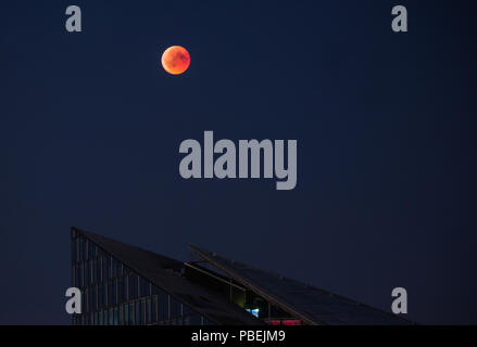 Frankfurt am Main, Germania. 27 Luglio, 2018. Il colore rosso-colorato la luna piena sorge sopra un impressionante edificio di uffici nelle principali metropoli. Durante la più lunga eclissi lunare del XXI secolo, la luna si tuffa nel cono d'ombra della Terra. Credito: Andreas Arnold/dpa/Alamy Live News Foto Stock