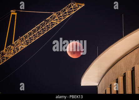 Frankfurt am Main, Germania. 27 Luglio, 2018. Tra una gru da cantiere e di un edificio nel centro della città, il rossastro colorato di luna piena può essere visto. Durante la più lunga eclissi lunare del XXI secolo, la luna si tuffa nel cono d'ombra della Terra. Credito: Frank Rumpenhorst/dpa/Alamy Live News Foto Stock