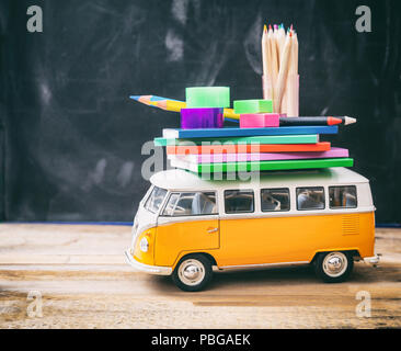 Si torna a scuola concetto. Forniture scolastiche e scuola bus sulla scrivania in legno, sfondo blackboard Foto Stock