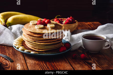 Pancake fatti in casa con fragole e fette di banana e la tazza di tè. Foto Stock