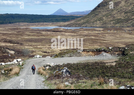 Lone uomo a camminare sulla strada per le isole con la montagna scozzese Munro Schiehallion in distanza, Rannoch, Highlands scozzesi, Scotland, Regno Unito. Foto Stock