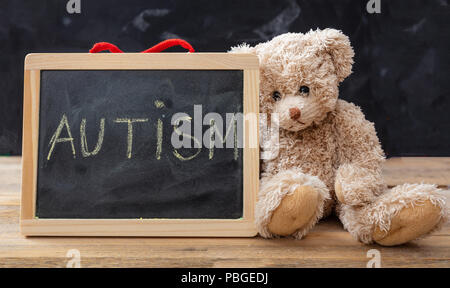 Autismo e scuola. Orsacchiotto di peluche e una lavagna. Testo di autismo disegno sulla lavagna Foto Stock