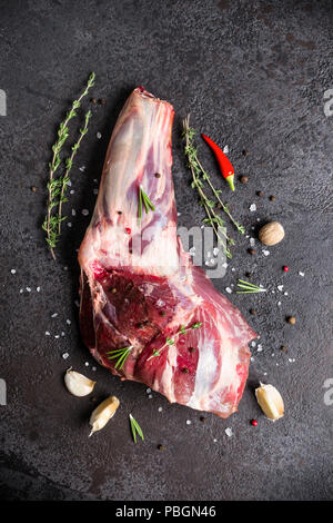 Crudo fresco di carne di agnello gambo e condimenti sulla pietra nera dello sfondo. Foto Stock