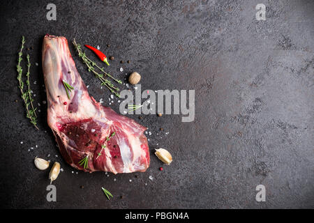 Crudo fresco di carne di agnello gambo e condimenti sulla pietra nera dello sfondo. Foto Stock