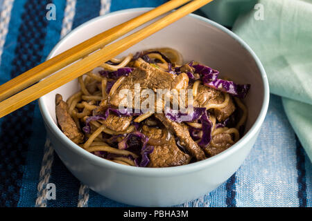 Bistecca, tagliatelle e cavolo viola closeup nella ciotola con bacchette - Pasto a base di noodle Foto Stock